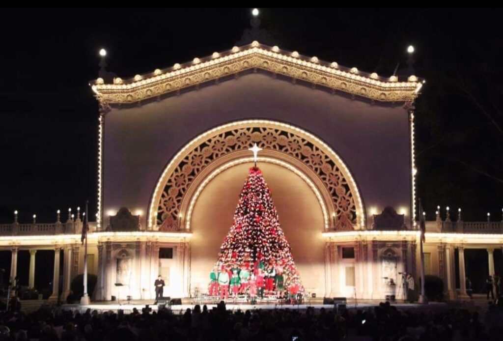 A lighted holiday tree with carolers at December nights in Balboa Park.